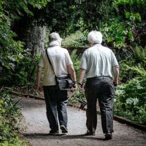 A senior couple walking hand in hand down a garden path. Knee pain relief for seniors who travel is the way to continue to enjoying life to its fullest.