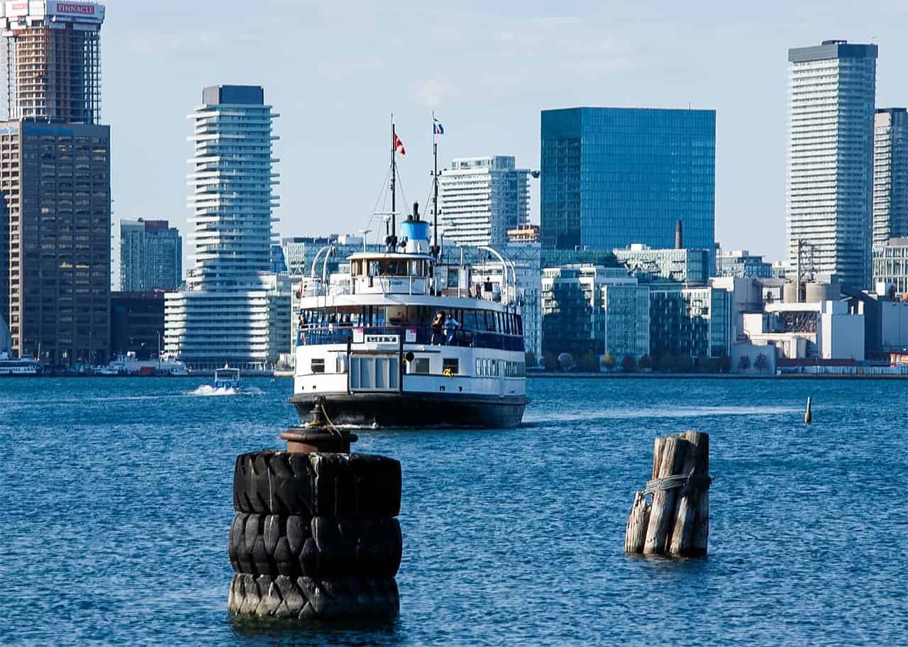 A ferry boat approaches the Toronto harbor with modern high-rise buildings in the background on a clear spring day. Calm waters and open seating make the scenic ride ideal for seniors enjoying relaxed spring travel in the city.