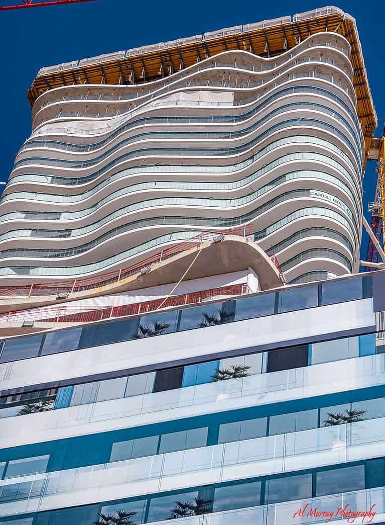 A modern high-rise building under construction in Monte Carlo, featuring wavy architectural lines and glass balconies that reflect the sky. A potential luxury stay option noted in a Monte Carlo Masters travel guide for seniors looking for elegant, accessible accommodations.