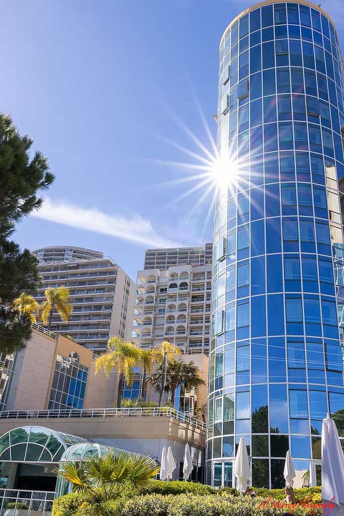 Tall modern buildings in Monte Carlo rise against a bright blue sky, with the sun reflecting off a glass-paneled tower. This sunny scene hints at upscale accommodations featured among the best hotels in Monte Carlo for seniors seeking comfort and style.