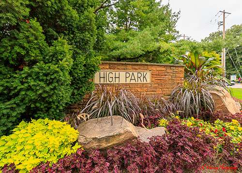 Entrance sign reading "HIGH PARK" set into a stone wall surrounded by lush greenery and colorful plants in bloom. This landscaped scene captures high park toronto in spring and summer with vibrant foliage and a welcoming garden entrance.