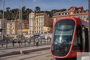 Red modern tram near the Port of Nice, with colorful historic buildings and docked sailboats in the background. This area is a senior-friendly place to visit in Nice, offering easy public transportation, scenic waterfront views, and accessible walking paths.