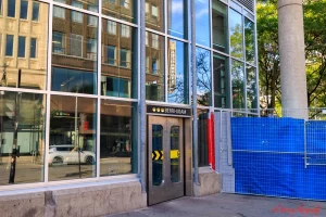 Street-level entrance to a hotel near Berri-UQAM metro station in Montreal, featuring wide glass doors, large windows, and level access, with nearby construction fencing partially visible. The image supports a review focused on finding the best hotel near Berri UQAM for seniors prioritizing convenience and accessibility.