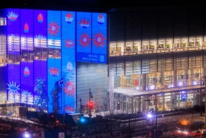 Vibrantly lit facade of the Bibliothèque et Archives nationales du Québec in downtown Montreal at night, with colorful digital displays and large glass windows glowing from within. This nearby landmark highlights the cultural and comfortable atmosphere around downtown Montreal hotels.