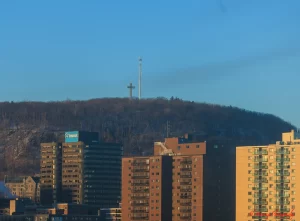 View of Mount Royal with its iconic cross overlooking mid-rise apartment buildings in downtown Montreal during golden hour. The image reflects the peaceful, residential feel of one of the best areas to stay in downtown Montreal for older adults seeking scenic views and a quieter atmosphere.