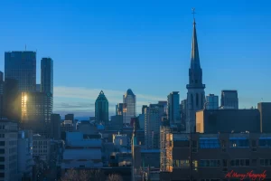 Early morning skyline of downtown Montreal featuring a church steeple and modern high-rises, including the sunlit Hyatt Place building on the left. The peaceful cityscape supports a Hyatt Place Montreal review aimed at senior travellers seeking a calm yet central location.