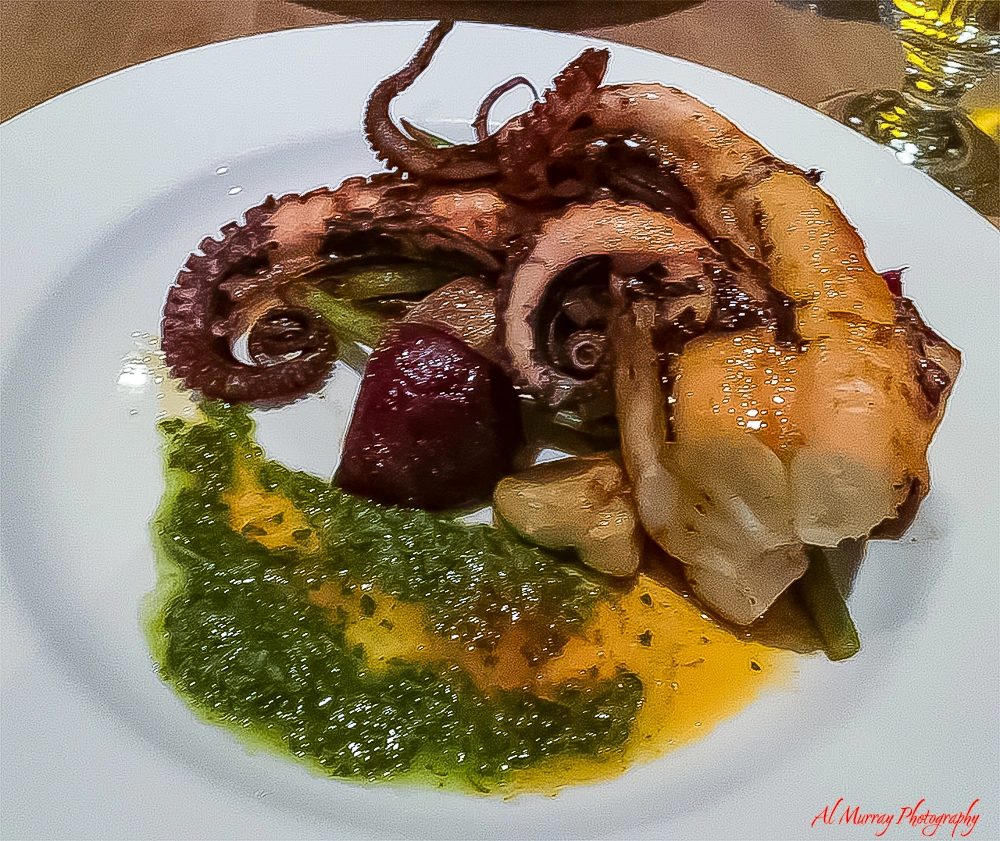 Plated seafood dish featuring a grilled octopus tentacle and large shrimp served over a bright green herb sauce with roasted vegetables and a beet garnish. The elegant presentation and vibrant colors showcase a standout entrée highlighted in this L Orignal restaurant Montreal review.