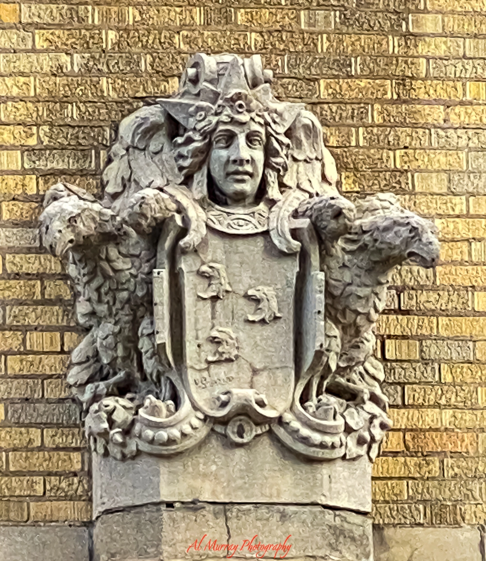 Stone crest sculpture on the facade of the building across from Hotel 2170 in Montreal, featuring a carved human face flanked by eagles and a shield with animal emblems. Historic architectural detail relevant to a hotel 2170 Montreal review for seniors seeking classic charm