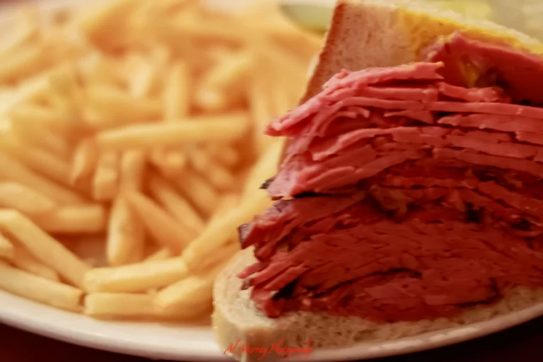 Close-up of a smoked meat sandwich stacked high with thin slices of juicy beef brisket on rye bread, served with a generous side of golden French fries. This classic deli plate highlights the famous smoke meat in Montreal.