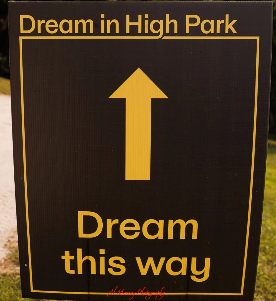 Black sign with yellow border reading "Dream in High Park" and "Dream this way" with an upward arrow pointing ahead. This directional sign adds a playful touch to the visitor experience and reflects why people ask is High Park Toronto worth visiting.