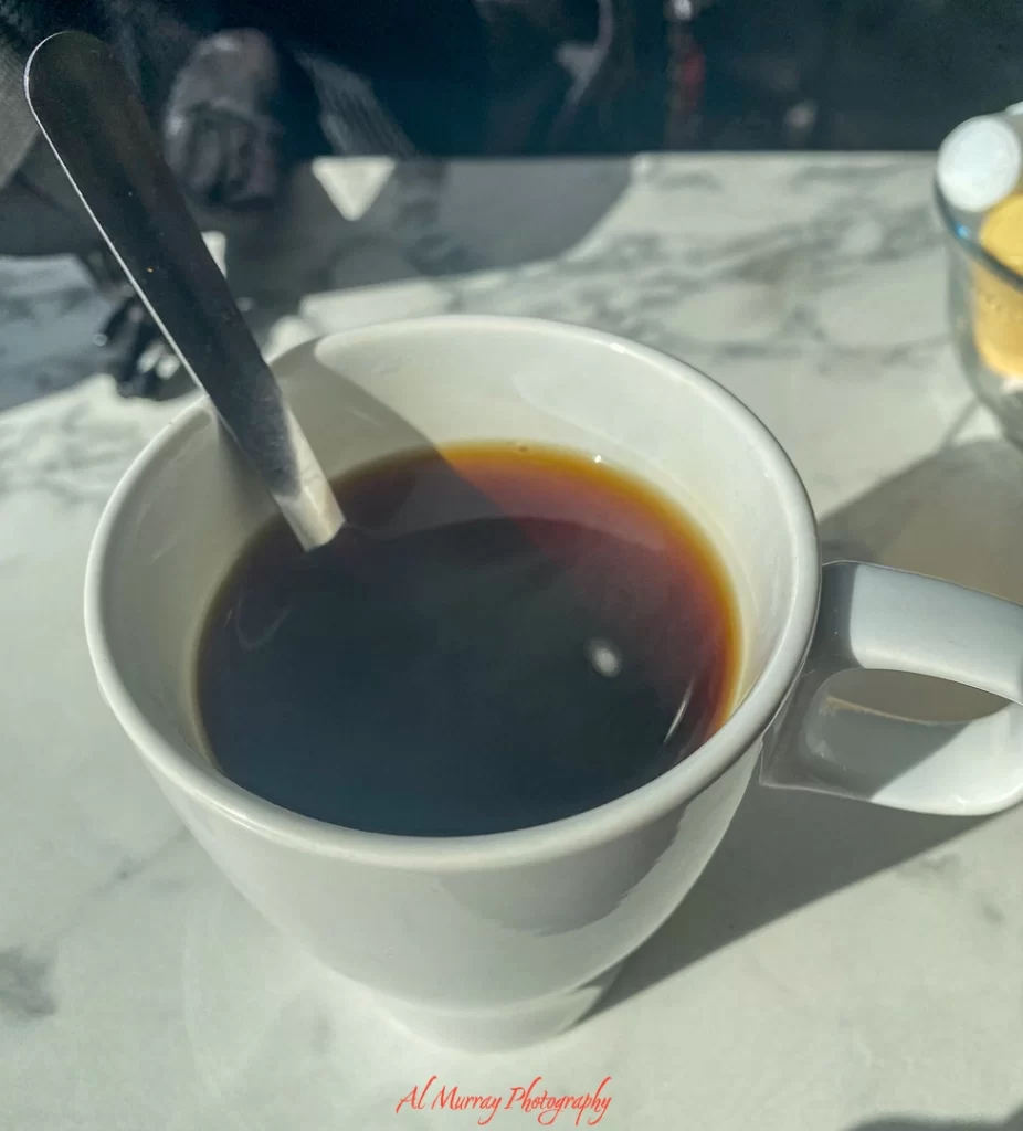 A steaming cup of black coffee in a white mug with a spoon inside, served on a marble table at Broadview Diner. The simple, no-fuss presentation reflects the comfortable and familiar vibe highlighted in a Broadview Diner review for seniors.