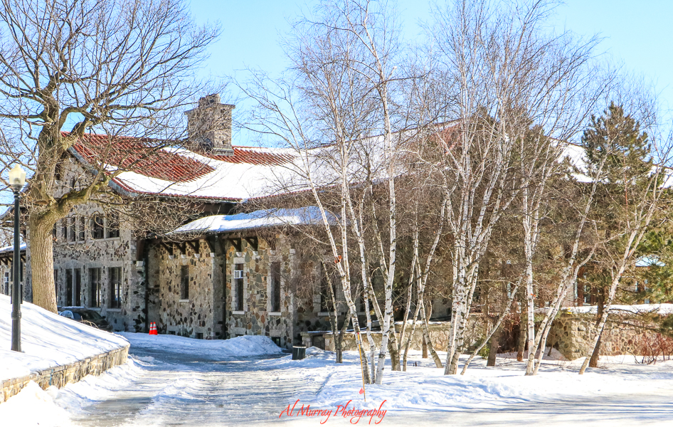 A rustic stone building with a red-tiled roof sits nestled among bare trees and snow-covered ground under a clear blue sky in Montreal. This cozy winter scene reflects the city’s historic charm and highlights the importance of seasonal awareness in any list of 9 Montreal travel tips.