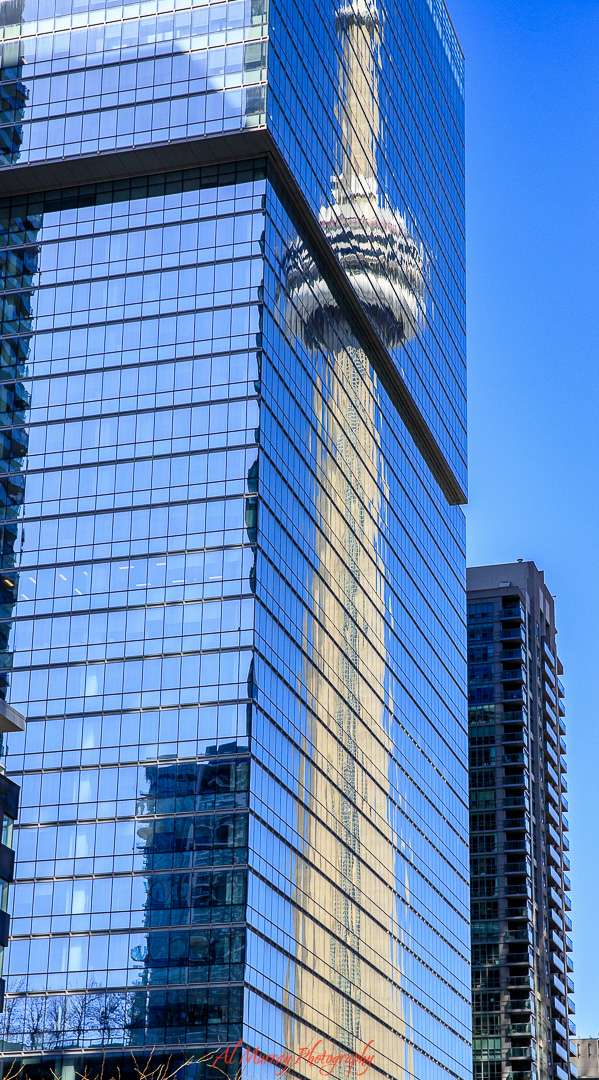Reflection of the CN Tower captured on the glass facade of a modern high-rise building in downtown Toronto. The clear blue sky and sharp architectural lines highlight the iconic landmark, offering a striking urban scene perfect for first-time visitors exploring the city. Visiting Toronto for the first time, the CN Tower is always a good direction guide.