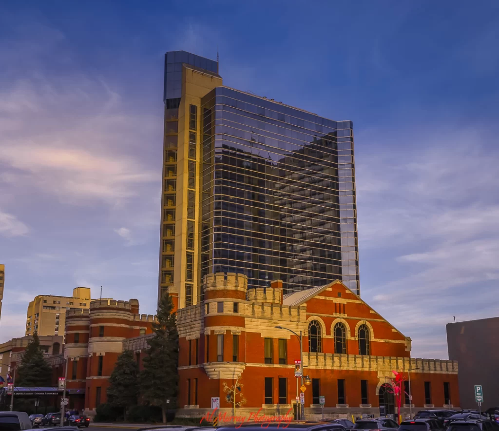 how to save money on toronto world cup 2026 hotels A striking blend of old and new architecture featuring a historic red-brick building with castle-like turrets in front of a modern glass high-rise, captured at golden hour in downtown Toronto. This area showcases the kind of affordable hotels near Toronto World Cup venues that offer both character and convenience.