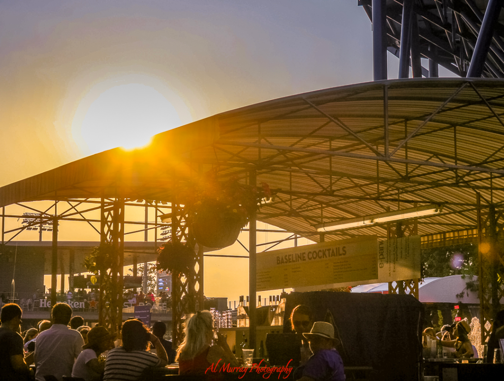 US Open travel guide for older tennis fans Golden hour sunlight bathes a shaded cocktail stand labeled “Baseline Cocktails” as attendees relax beneath the canopy at the US Open. This inviting atmosphere illustrates one of the more comfortable spots to unwind, ideal for US Open tips for seniors looking to avoid peak sun and crowds.