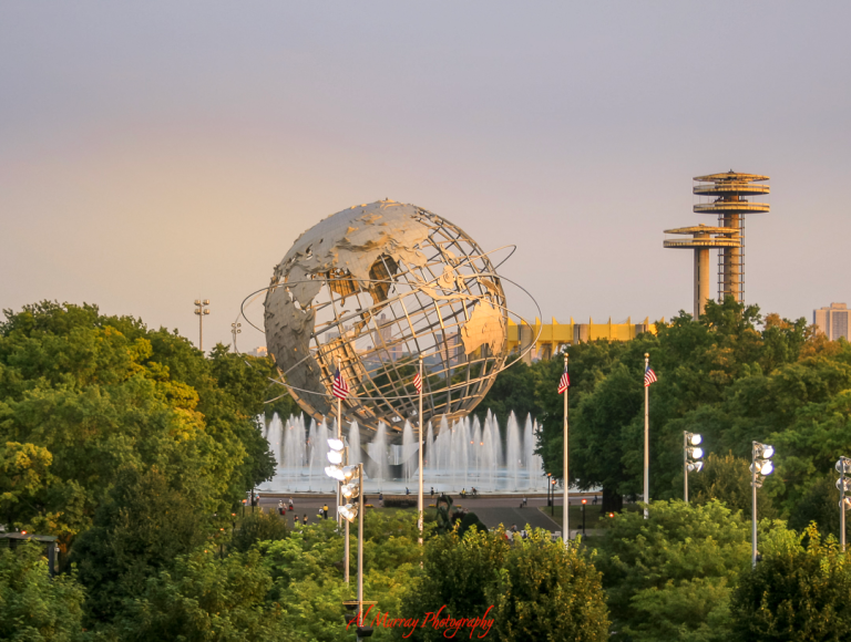 The iconic Unisphere sculpture in Flushing Meadows–Corona Park stands surrounded by fountains and lush greenery at sunset, with observation towers from the 1964 World’s Fair in the background. This scenic landmark is a peaceful nearby attraction perfect for a stroll, featured in many US Open travel guides for older tennis fans.