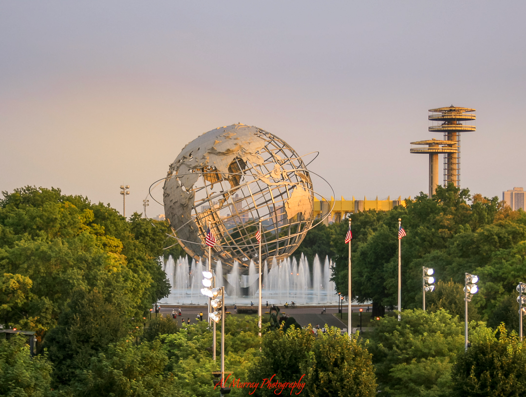 The iconic Unisphere sculpture in Flushing Meadows–Corona Park stands surrounded by fountains and lush greenery at sunset, with observation towers from the 1964 World’s Fair in the background. This scenic landmark is a peaceful nearby attraction perfect for a stroll, featured in many US Open travel guides for older tennis fans.