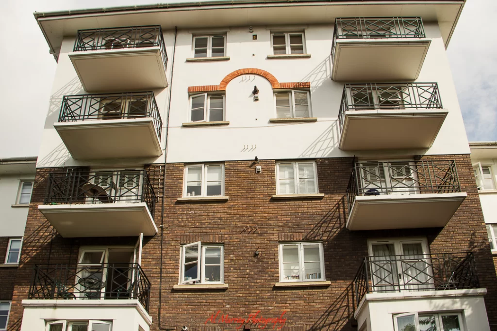 Exterior of a brick and white-painted apartment building in London with five floors, black metal balconies, and evenly spaced windows. This is the exterior of our Airbnb in London. This image adds visual context to a Wimbledon guide for mature travellers exploring accommodation styles in the area.