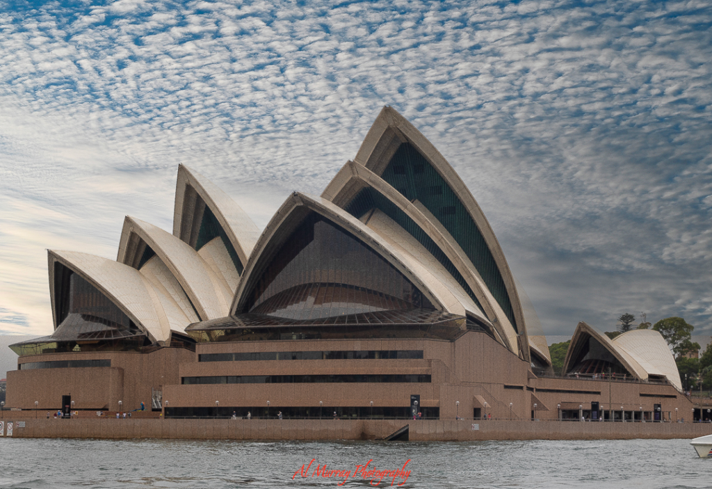 Close-up view of the Sydney Opera House with its iconic sail-like roofs under a textured sky, symbolizing Australia's cultural backdrop that enriches the Australian Open tennis tips for fans exploring more than just the tournament. The water in the foreground adds to the scenic coastal charm.