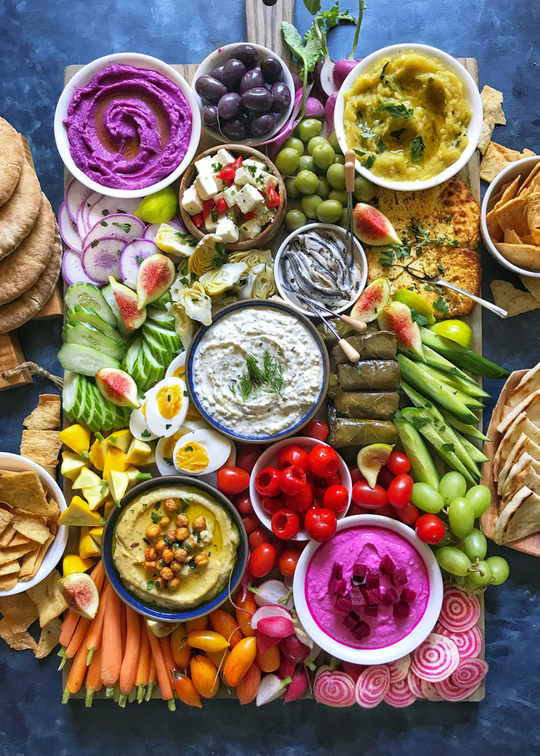 Colorful Mediterranean mezze platter featuring hummus, tzatziki, olives, feta, cucumbers, grape leaves, pita, and vibrant fresh vegetables like carrots, tomatoes, figs, and radishes. This vibrant spread visually captures the variety and balance emphasized in Mediterranean diet 101 for beginners.