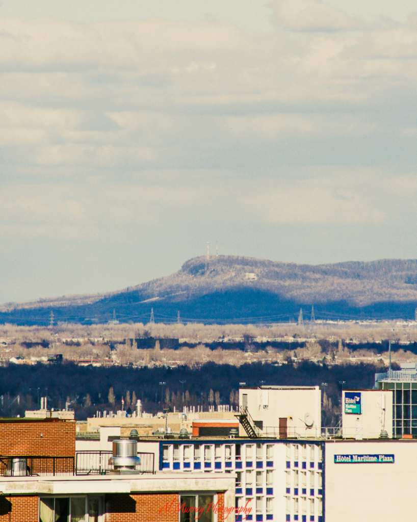 Distant view of Colline d"Outremonte rising beyond Montreal’s cityscape, framed under a soft winter sky with the Hotel Maritime Plaza sign visible in the foreground. This scenic overlook adds a peaceful pause to any Montreal Valentine’s Day itinerary for couples.
