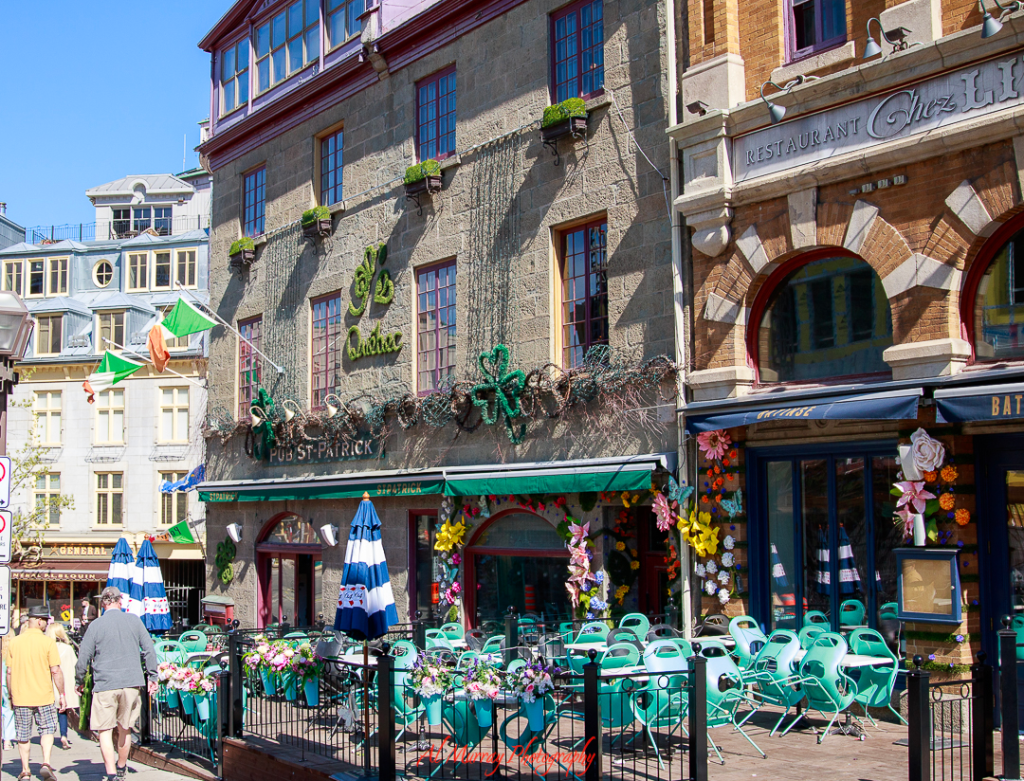 Colorful storefronts and quaint outdoor seating line a cobblestone street in Old Quebec, with flower decorations and vintage charm creating a cozy atmosphere. This tucked-away corner is one of the quiet romantic spots in Quebec City, perfect for a peaceful café date or leisurely stroll.

