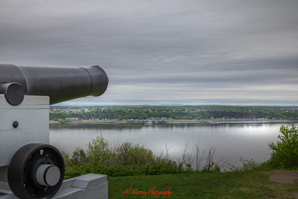 An old cannon overlooks the St. Lawrence River from a grassy bluff under a cloudy sky, with a peaceful view of the shoreline across the water. This scenic viewpoint adds a quiet, historic touch to a Quebec City Valentine’s Day itinerary for 3 days, ideal for a reflective romantic walk.
