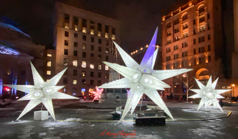 Illuminated star-shaped sculptures glow in a Montreal plaza at night, surrounded by historic buildings and patches of snow. This romantic winter light display offers a magical backdrop for couples exploring a Montreal Valentine's Day itinerary.
