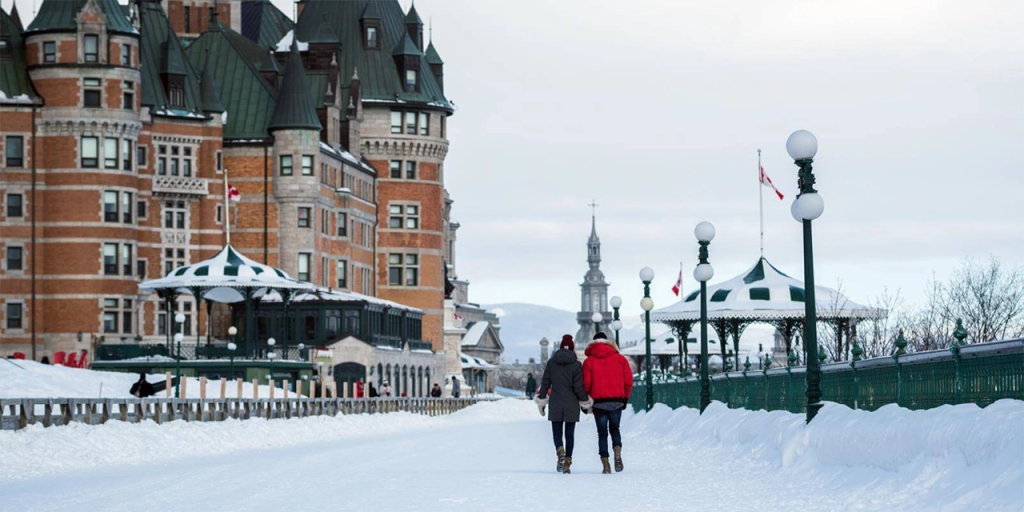 Couple walks hand-in-hand through a snow-covered promenade in front of the iconic Château Frontenac in Quebec City, surrounded by vintage lamp posts and gazebo-style pavilions. The fairytale architecture and wintry charm make this one of the most romantic places in Canada for Valentine’s Day.