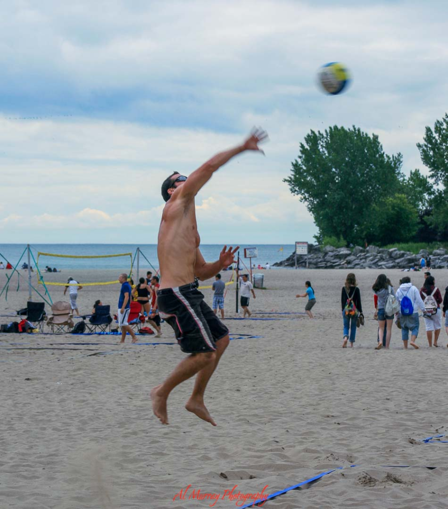 where to watch the world cup 2026 in vancouver Man jumping to spike a volleyball on a sandy Vancouver beach with other players, nets, and Lake water visible in the background under a cloudy sky. The energetic beach scene highlights fun things to do during Vancouver World Cup 2026, from outdoor sports to soaking up the city’s lively summer atmosphere between matches.