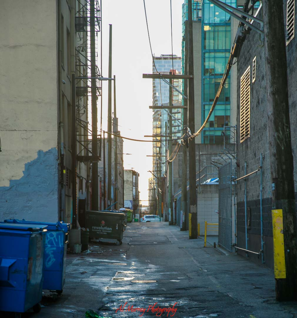 where to watch the world cup 2026 in vancouver Narrow downtown Vancouver alley with dumpsters, overhead power lines, and tall buildings on either side leading toward brighter high rise towers in the distance. The urban back lane setting reflects the hidden spots and nearby neighborhoods where fans might watch World Cup near BC Place, just steps from the stadium buzz.