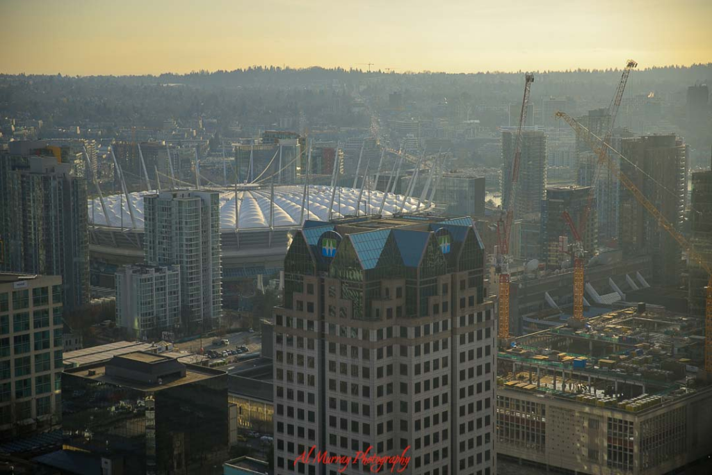 where to watch the world cup 2026 in vancouver Aerial view of downtown Vancouver at sunset with BC Place stadium’s white roof visible among high rise towers and construction cranes under a hazy golden sky. The cityscape sets the scene for where to watch World Cup 2026 in Vancouver, highlighting the vibrant downtown core near the main stadium and fan gathering areas.