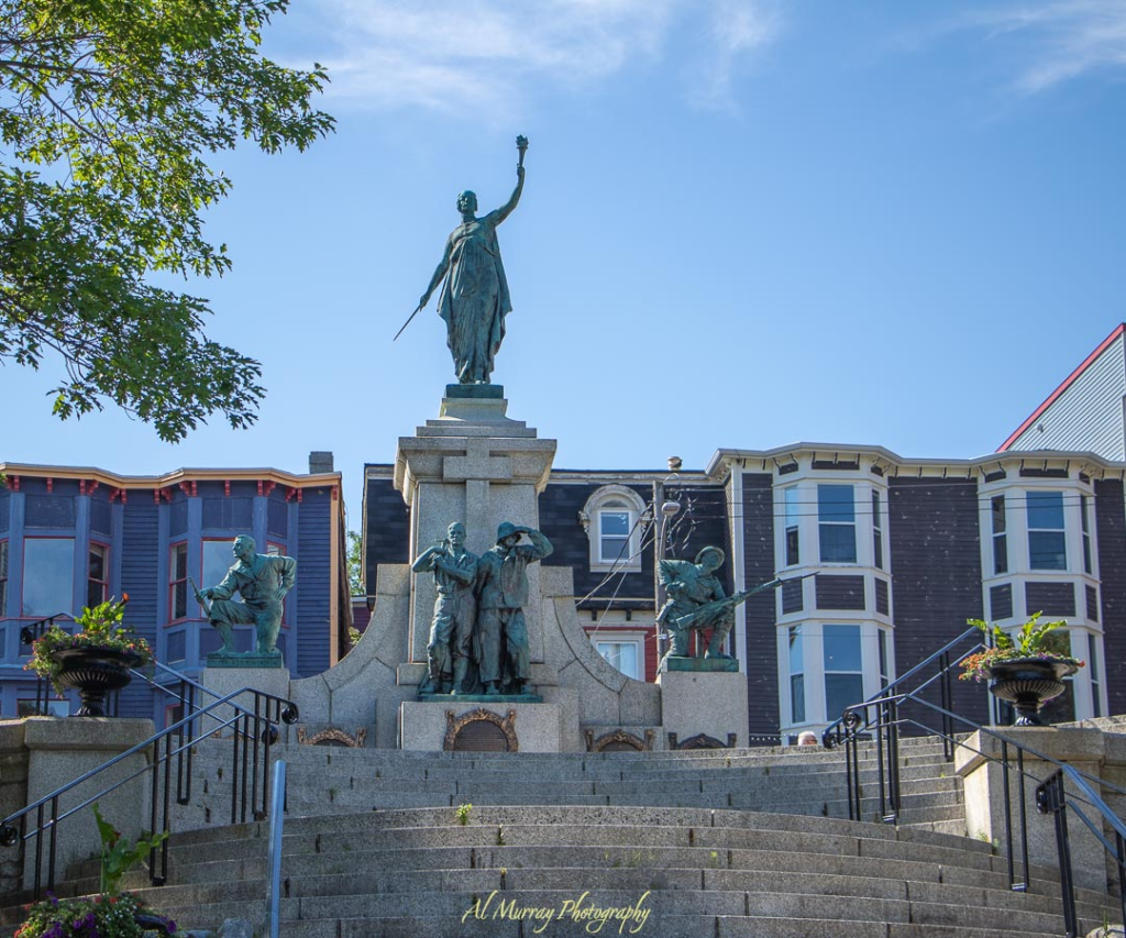 The National War Memorial in downtown St. John’s stands tall with bronze soldier statues and a female figure atop granite steps, framed by historic row houses and a clear blue sky. This easily accessible landmark is a meaningful and senior-friendly travel stop in Newfoundland.