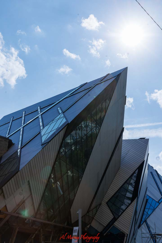 where to watch the world cup 2026 in Toronto Sharp angular glass and metal facade of the Royal Ontario Museum in Toronto viewed from below against a bright blue sky with scattered clouds. The dramatic modern architecture highlights one of the top Things to do in Toronto during World Cup 2026, offering visitors a striking cultural experience between matches.