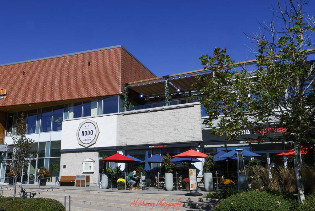 where to watch the world cup 2026 in Toronto Modern two story commercial building in Toronto with a NODO Liberty sign on a white brick facade and a street level patio featuring red and blue umbrellas and outdoor seating under a clear blue sky. The lively restaurant patio setting reflects popular spots locals and visitors might consider when deciding Where to Watch the World Cup 2026 in Toronto.