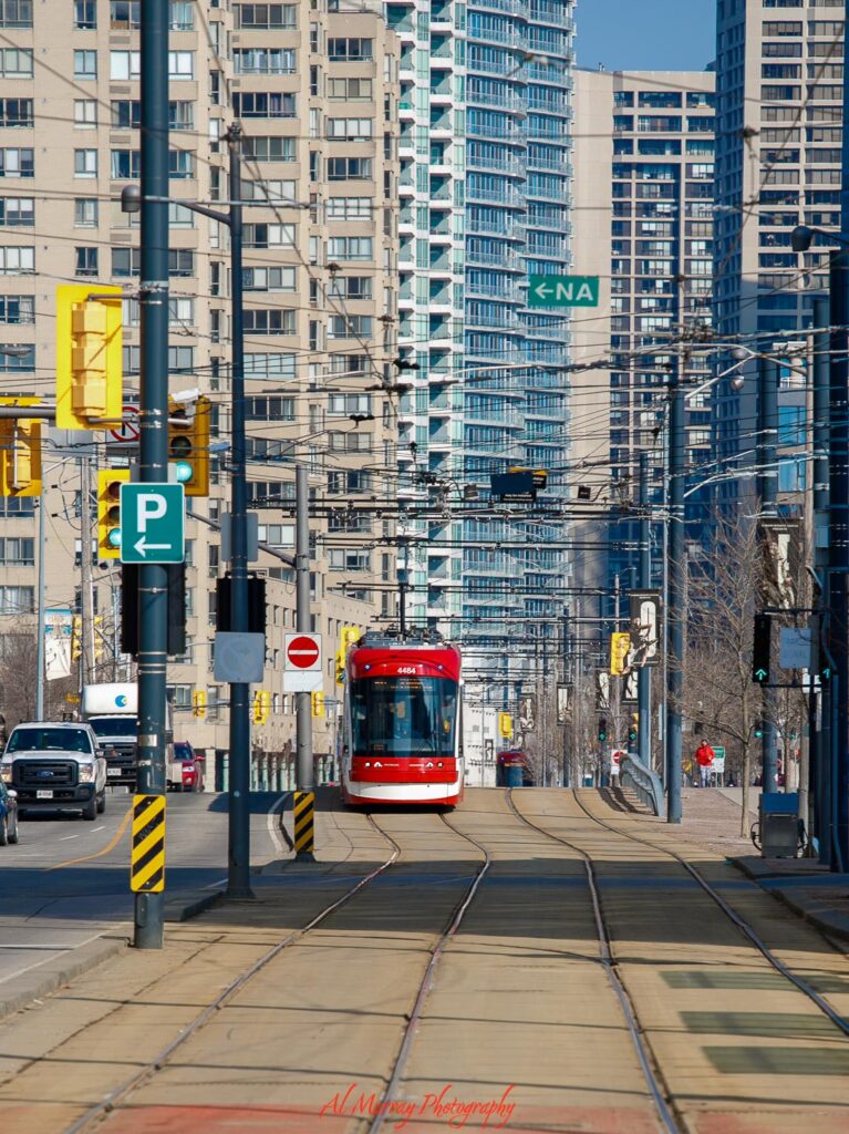 Red streetcar traveling along tracks through a busy downtown Toronto street with tall buildings and overhead wires, showing an accessible way to get around highlighted in toronto public transit tips.