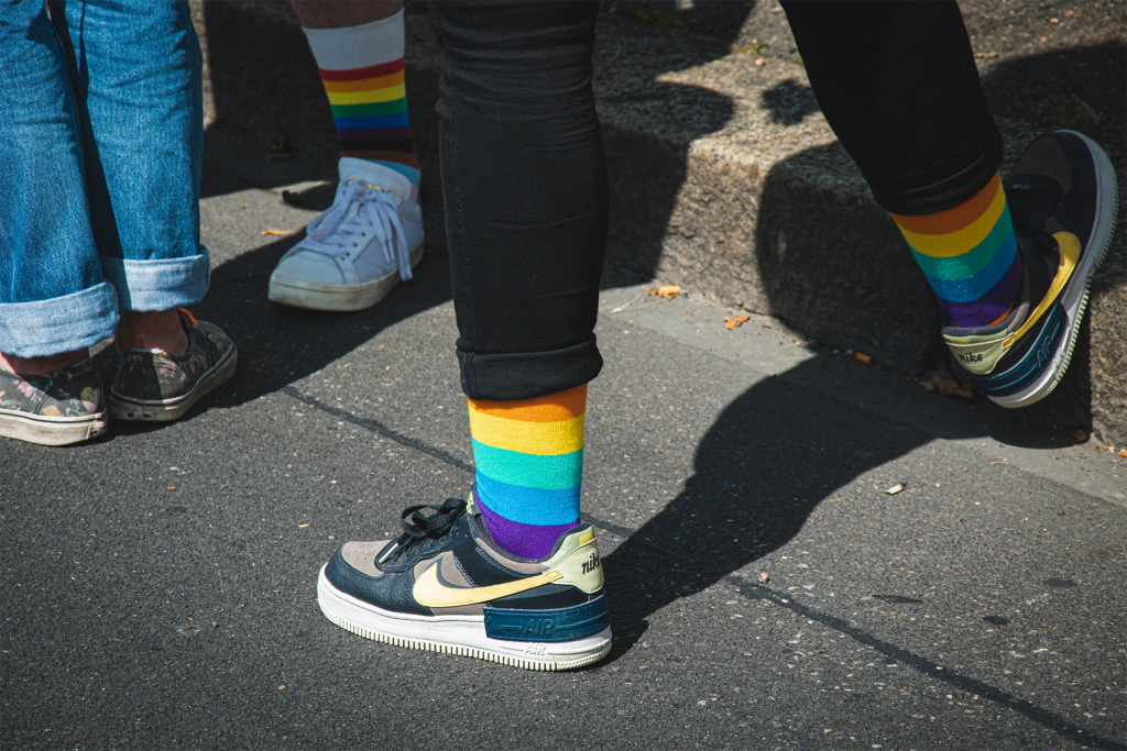 Three people walking up outdoor steps wearing rainbow striped socks and sneakers on a sunny day. The colorful pride apparel reflects the inclusive spirit travelers can experience during LGBTQ travel Canada spring summer trips.