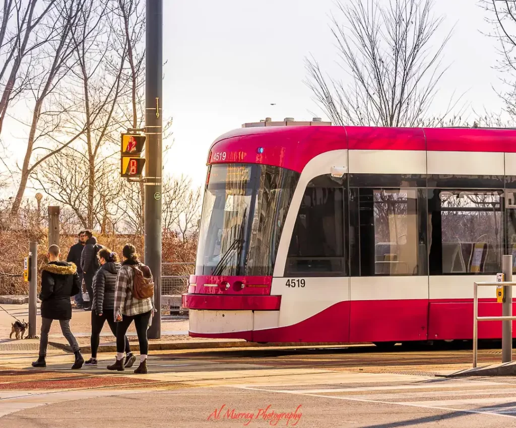 Red and white Toronto streetcar stopped at a crosswalk as pedestrians walk past in a neighborhood setting, illustrating best areas to stay in toronto without a car with easy access to transit and walkable streets.
