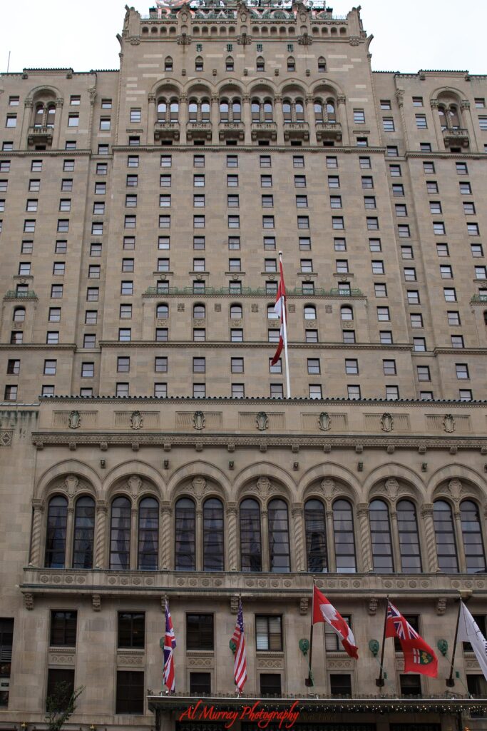 Historic Fairmont Royal York hotel facade in downtown Toronto with rows of arched windows and ornate stone detailing. Canadian and international flags line the entrance, representing a landmark stay option when exploring Toronto hotels by neighbourhood.