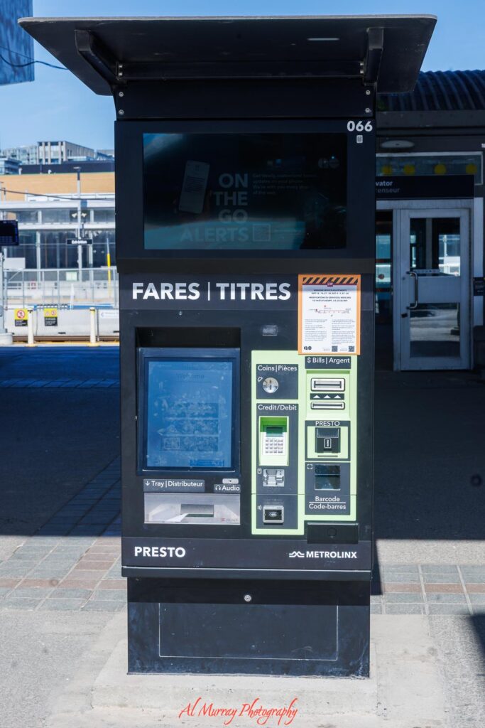 Black PRESTO fare machine at a Toronto transit station with screen and payment options labeled "FARES TITRES", "Coins Pièces", "Credit Debit", "Bills Argent", and "Barcode Code barres". Public transit access like this helps visitors navigate between areas when staying at Toronto hotels by neighborhood.