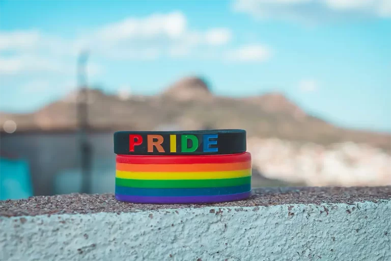 Stack of rainbow silicone wristbands sitting on a stone ledge with the word "PRIDE" in colorful letters on the top band. The bright colors and pride message reflect the welcoming atmosphere travelers can find during LGBTQ travel Canada spring summer experiences.