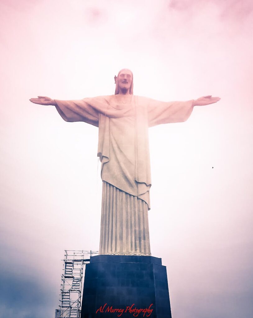 Christ the Redeemer statue rises above a misty pale pink sky with both arms outstretched in a welcoming pose. The soft haze and towering monument create a serene scene that captures the grandeur and wonder often felt during an Atlantic Crossing Cruise Experience.