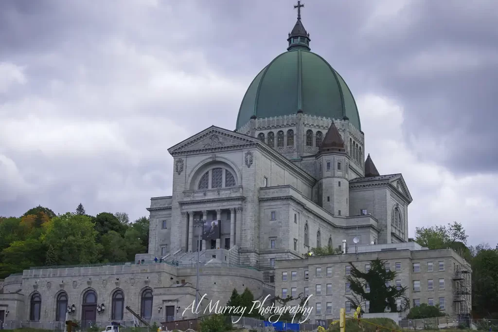 Saint Joseph’s Oratory of Mount Royal in Montreal rises beneath a cloudy sky with its massive green copper dome and pale stone facade. The landmark is a notable stop while exploring Montreal Quebec City Ottawa by train and the watermark reads "Al Murray Photography".