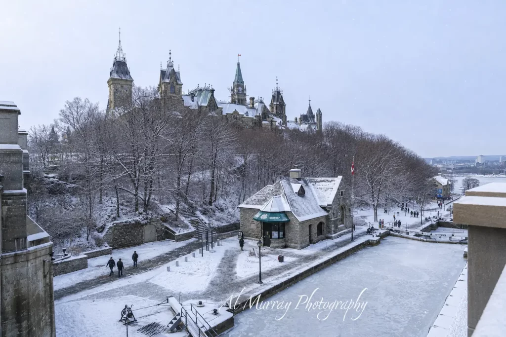 Snow covers the Rideau Canal locks in Ottawa with the Bytown Museum beside the frozen water and the Parliament Hill buildings rising above the trees. The wintry landmark scene suits an Eastern Canada winter itinerary and the watermark reads "Al Murray Photography".