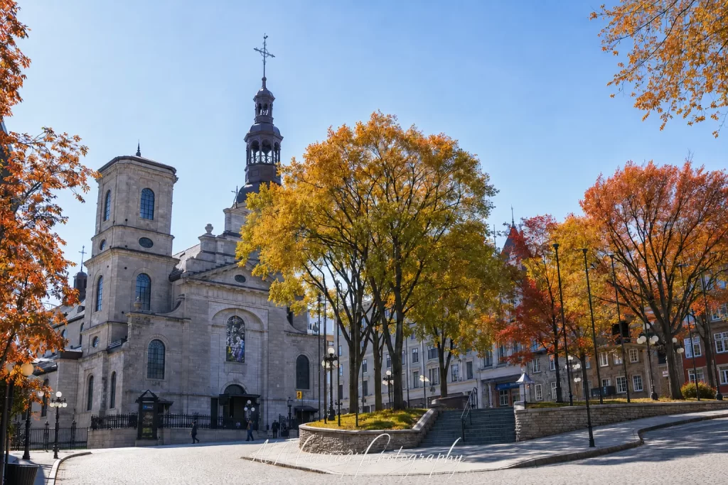 Notre Dame de Quebec Basilica Cathedral stands beside City Hall Square in Quebec City with yellow orange and red autumn trees glowing beneath a clear blue sky. This historic Old Quebec landmark adds fall scenery and architecture to a Montreal Quebec City and Ottawa itinerary and the watermark reads "Al Murray Photography"