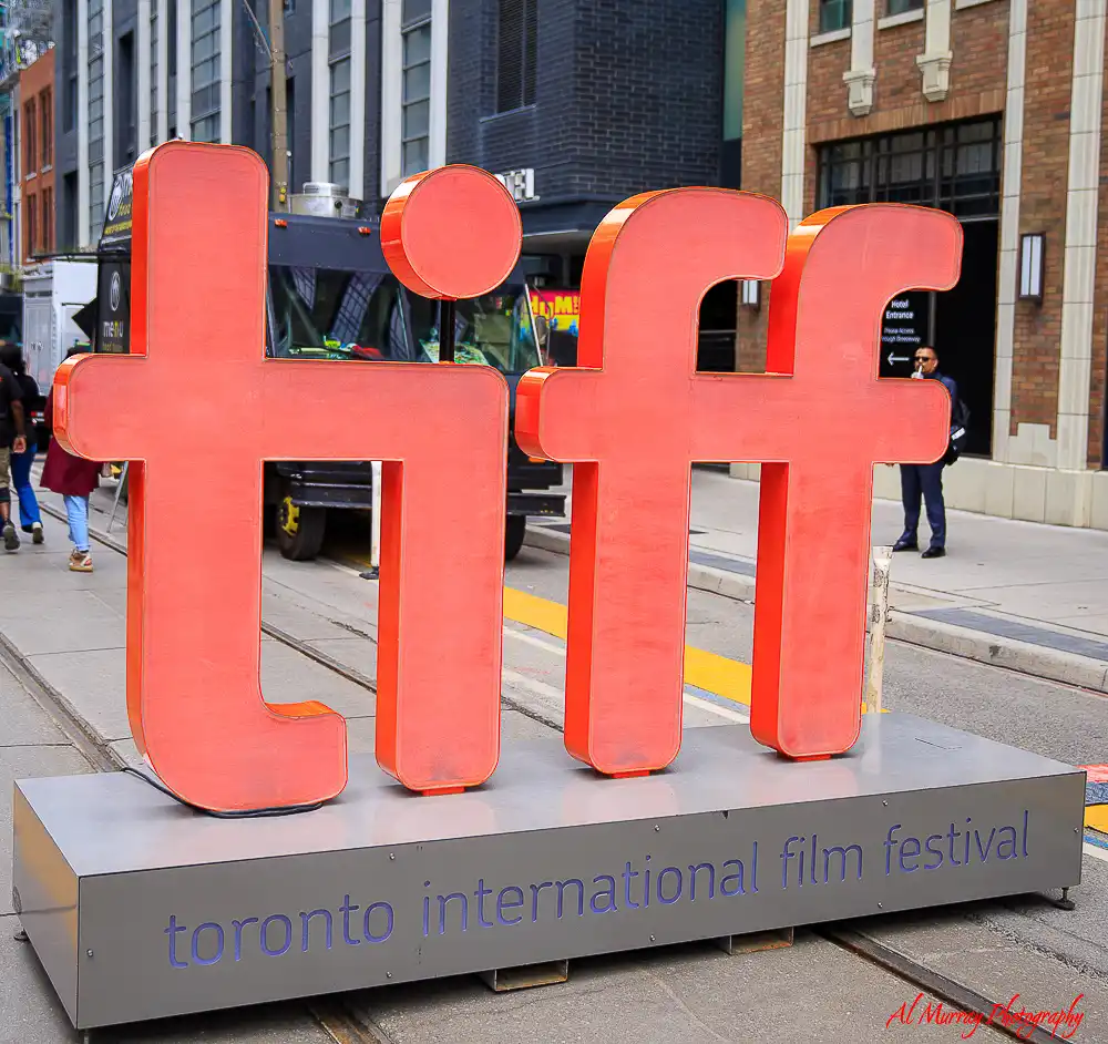 Large red letters spelling “tiff” stand on a downtown Toronto street with streetcar tracks and brick buildings behind them. The base reads “toronto international film festival” and highlights one of the popular things to do in Toronto in the fall.