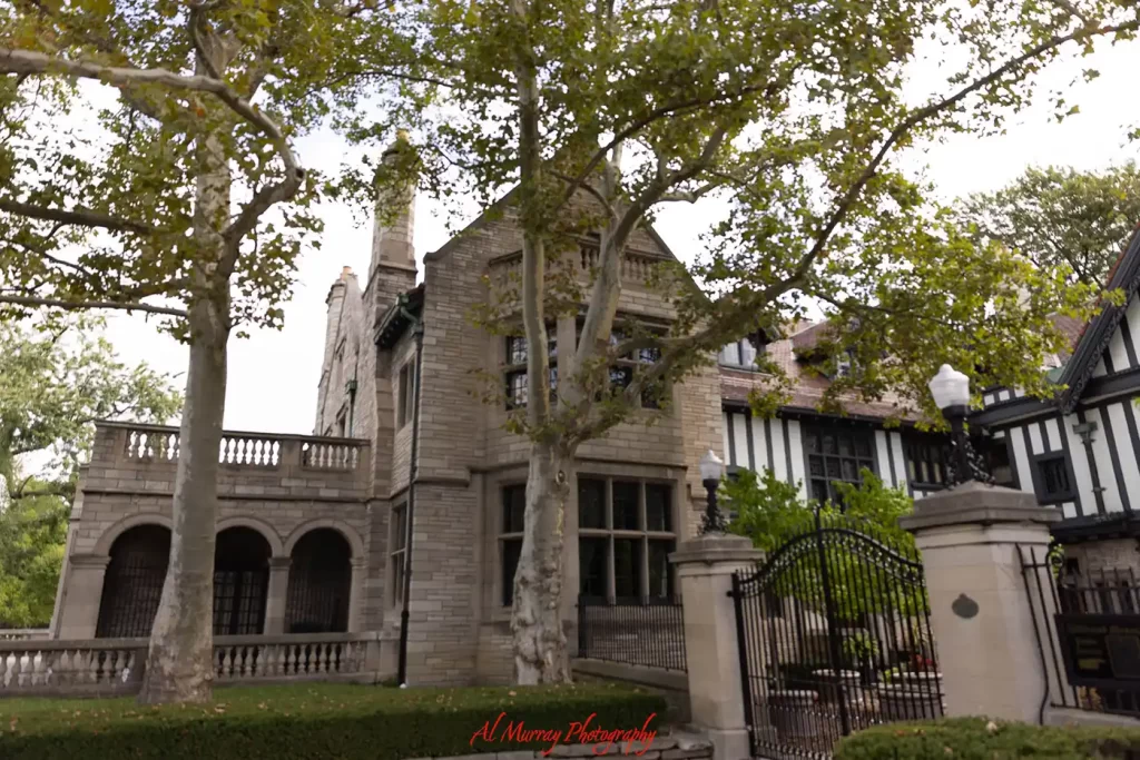 A grand stone and Tudor style mansion stands behind mature trees and a black wrought iron gate during Windsor Essex winter getaways. Arched terraces tall chimneys and the red watermark "Al Murray Photography" are visible
