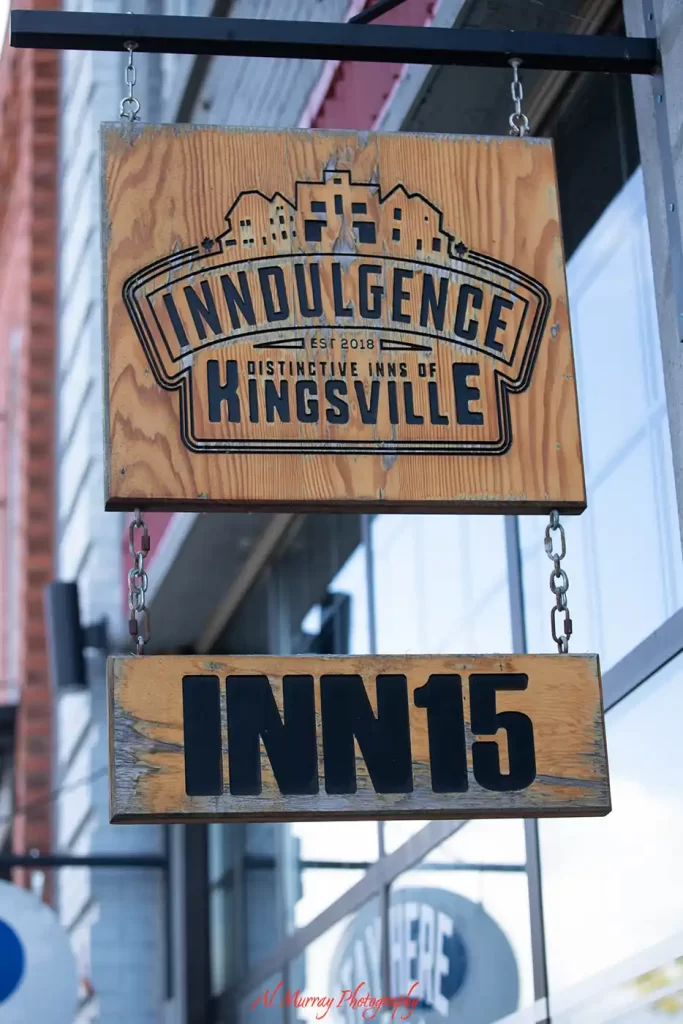 Rustic wooden signs hang outside a building and read "INNDULGENCE. EST 2018. DISTINCTIVE INNS OF KINGSVILLE." and "INN15." The boutique inn sign highlights a place to stay while exploring Kingsville wineries and includes the red watermark "Al Murray Photography".