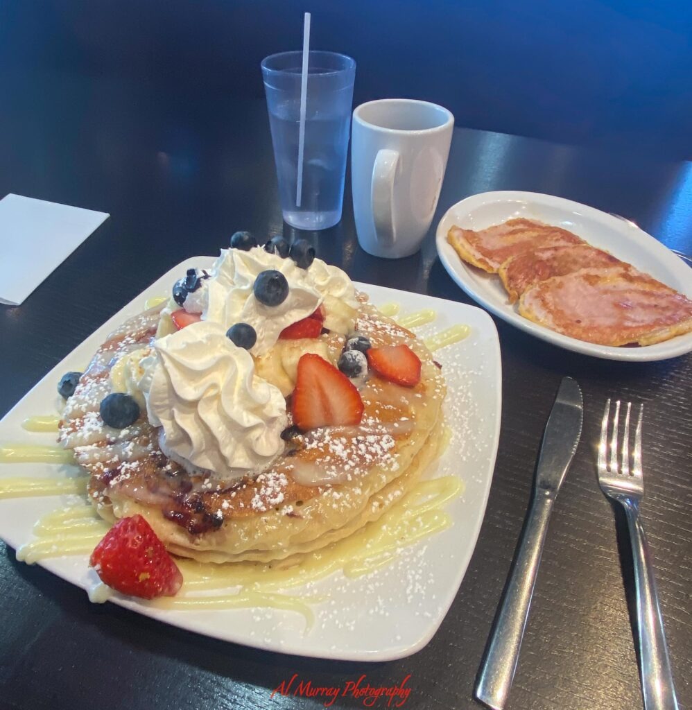 toronto hotels with breakfast included A breakfast spread features a stack of pancakes topped with whipped cream strawberries blueberries powdered sugar and a sweet drizzle beside slices of grilled ham and a mug of coffee. The colorful meal captures the kind of hearty morning feast travelers may picture when searching for Toronto hotels with breakfast included. The red watermark reads "Al Murray Photography".