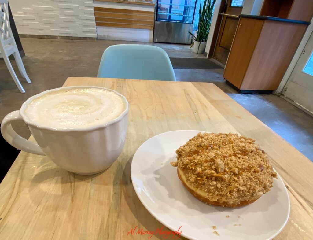 toronto hotels with breakfast included A large mug of frothy coffee sits beside a crumb topped pastry on a white plate at a bright wooden cafe table. The cozy breakfast scene adds a relaxed morning moment to a guide about Toronto hotels with free breakfast. The red watermark reads "Al Murray Photography"